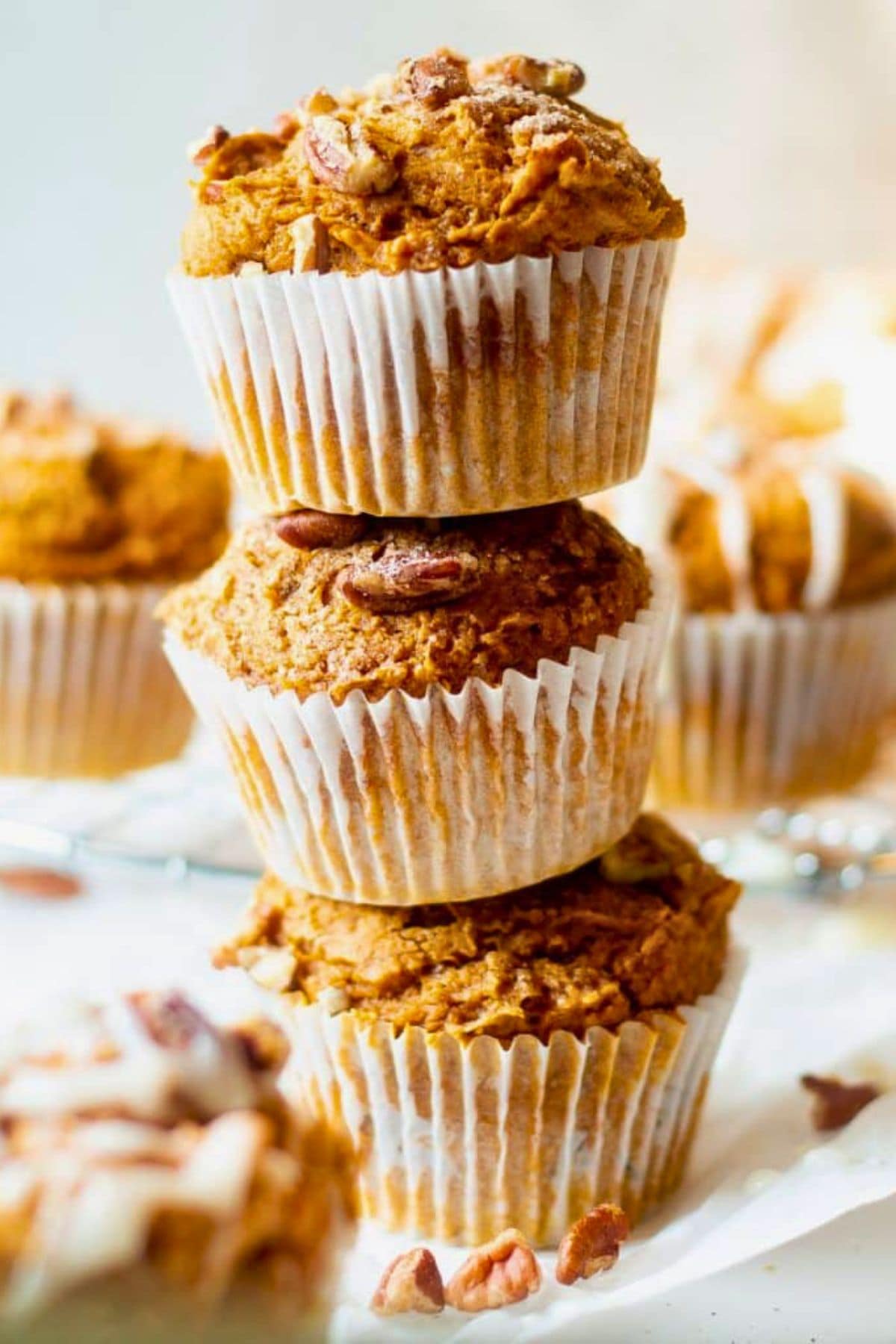 Three pumpkin muffins stacked on top of each other with pecan pieces on top.