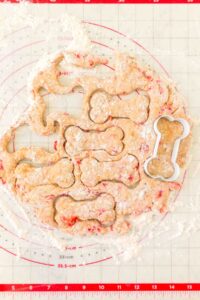 Bone-shaped cookie cutters pressed into dough on a floured baking mat.