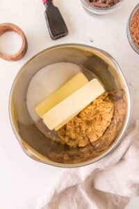 A mixing bowl with butter, brown sugar, and white sugar on a white surface.