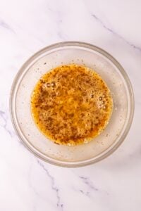 Clear bowl with whisked eggs and spices on a white marble surface.
