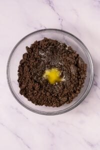 A glass bowl with crushed Oreo and melted butter on top.