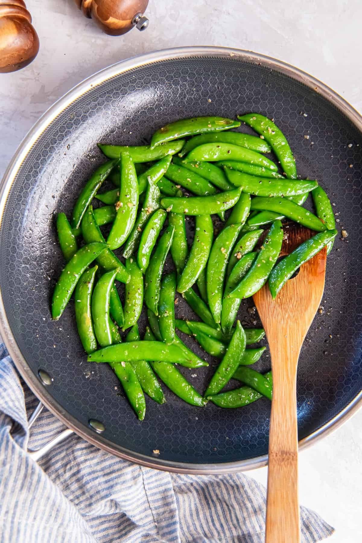 Snap peas being saut&eacute;ed, perfect for fresh spring vegetable recipes.