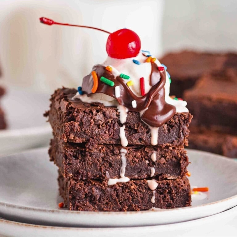 A stack of brownies topped with ice cream, chocolate sauce, sprinkles, and a cherry.