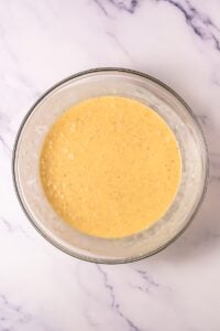 Glass bowl with yellow sauce mixture on a white marble surface.