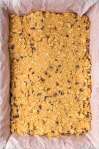 Unbaked oatmeal cookie bars with chocolate chips in a parchment-lined pan.