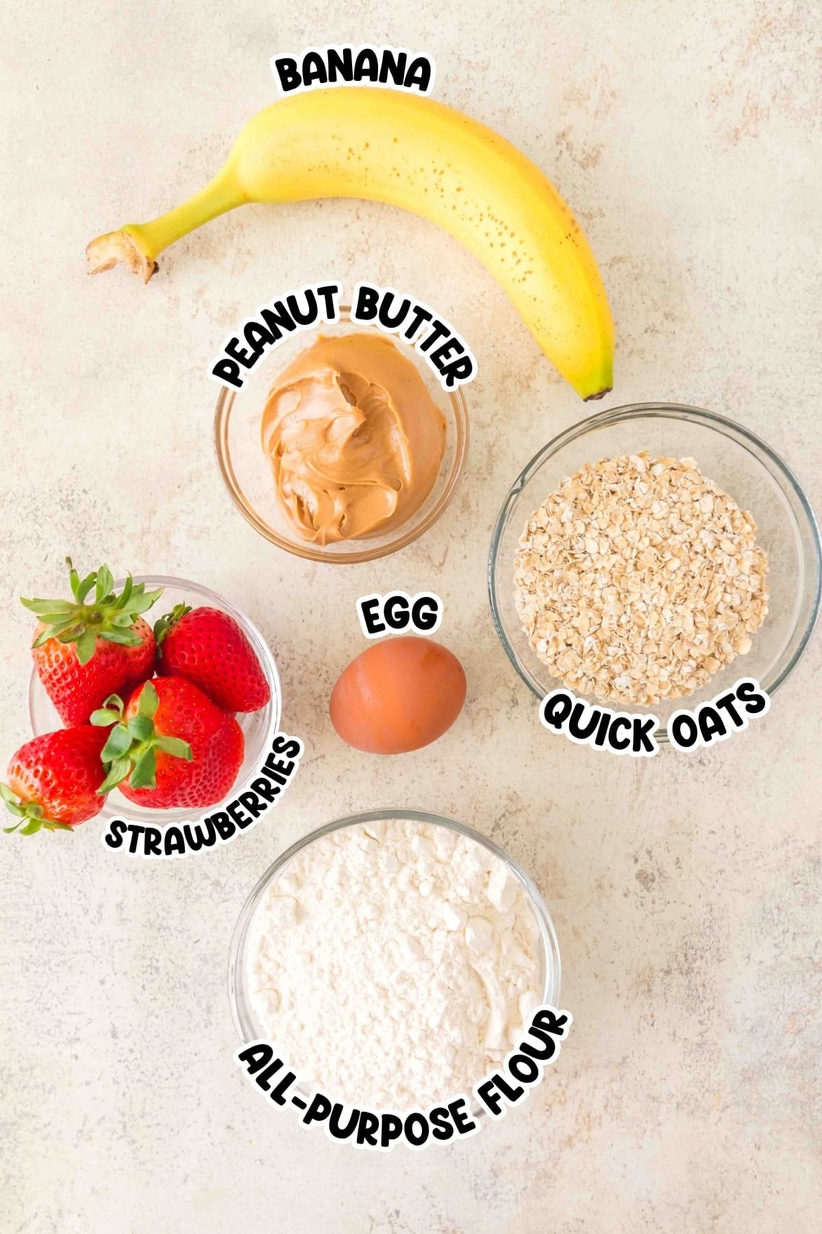 Banana, peanut butter, quick oats, strawberries, egg, and flour on a table.