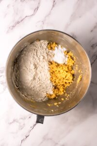 Mixing bowl with flour, baking powder, and mashed banana on a marble surface.