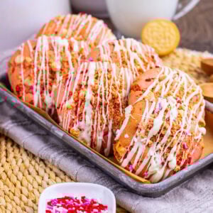Six cookies with white icing drizzle and sprinkles on a baking tray.