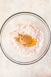 A glass bowl with flour, peanut butter, and an egg on a light surface.