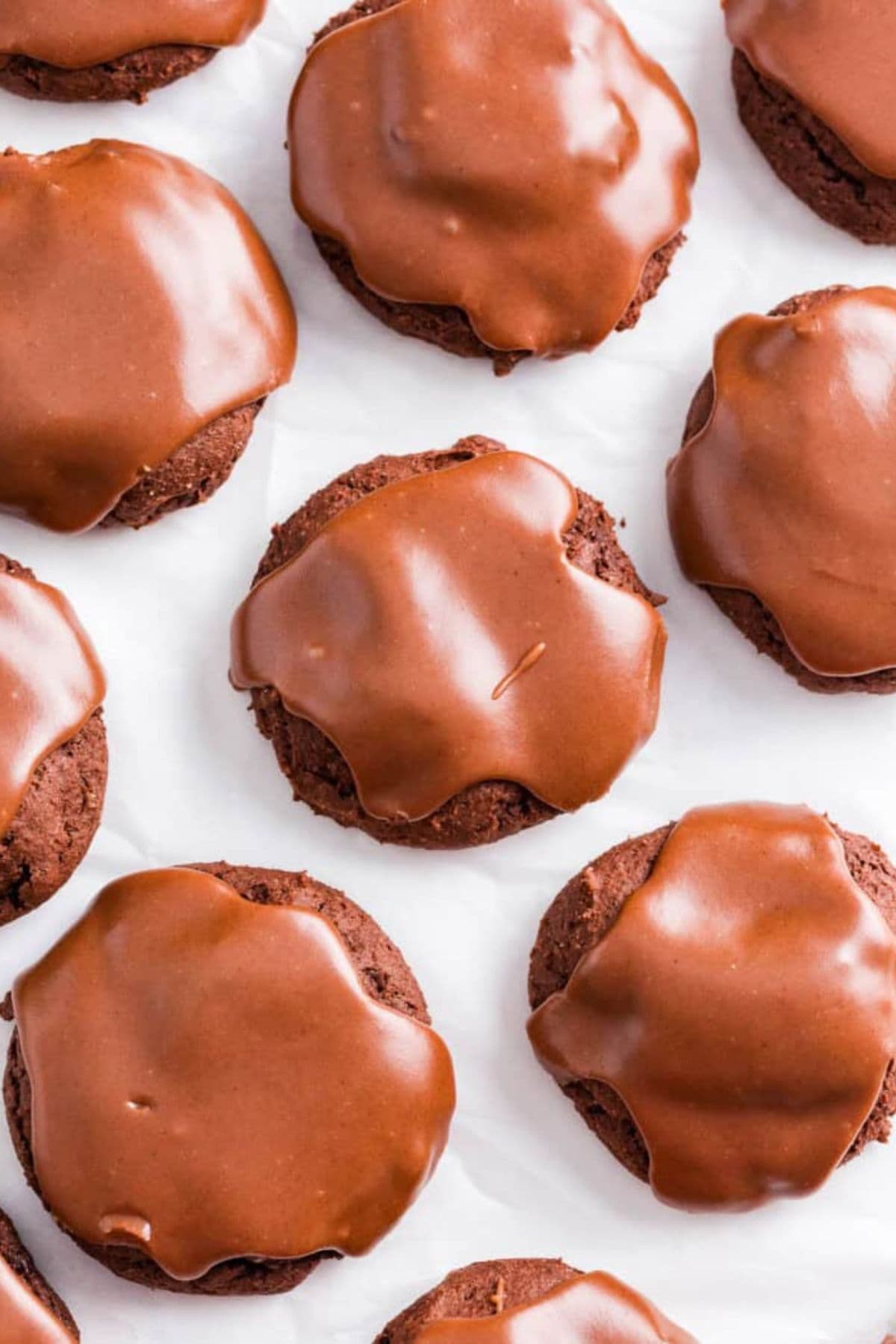 Chocolate cookies topped with smooth chocolate glaze, arranged on a white surface.