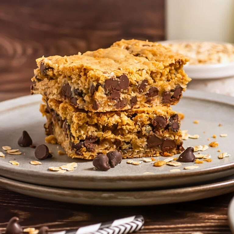 Two oat and chocolate chip bars stacked on a plate with scattered oats and chips.