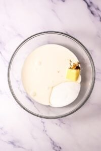 Glass bowl with cream, sugar, butter, and vanilla on a marble surface.