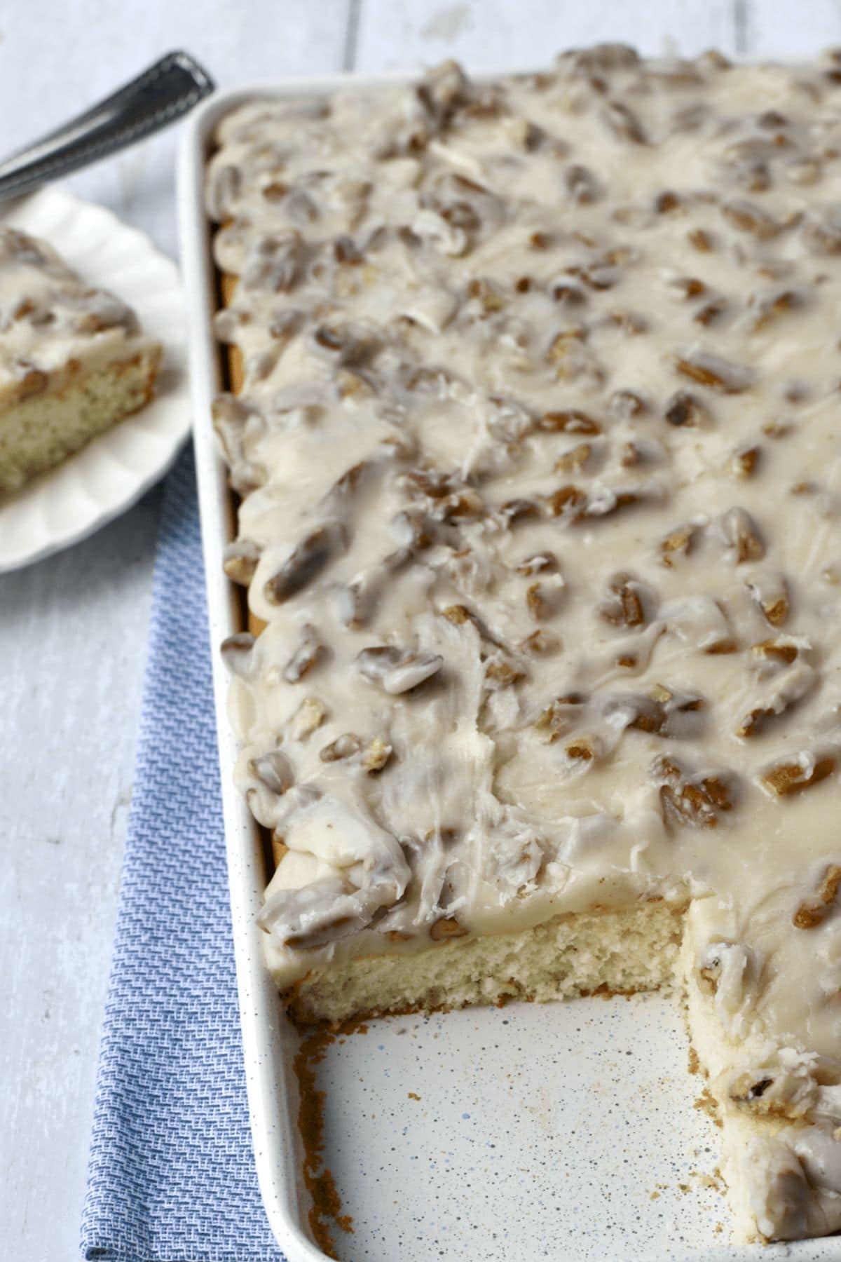 Sheet cake with white icing and pecans, one piece served on a plate nearby.