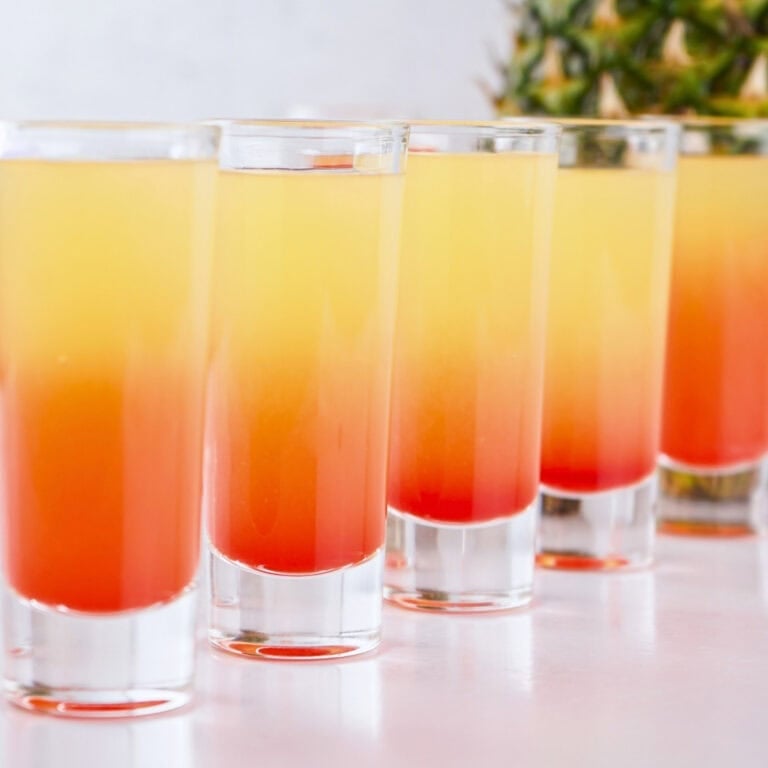 Five layered orange and yellow shots in clear glasses on a white surface.