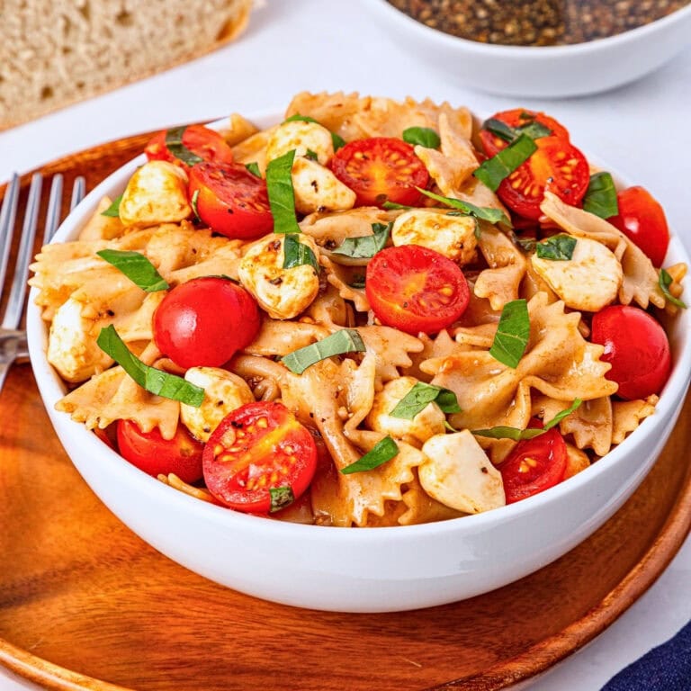 Pasta salad with cherry tomatoes, mozzarella, and basil in a white bowl.