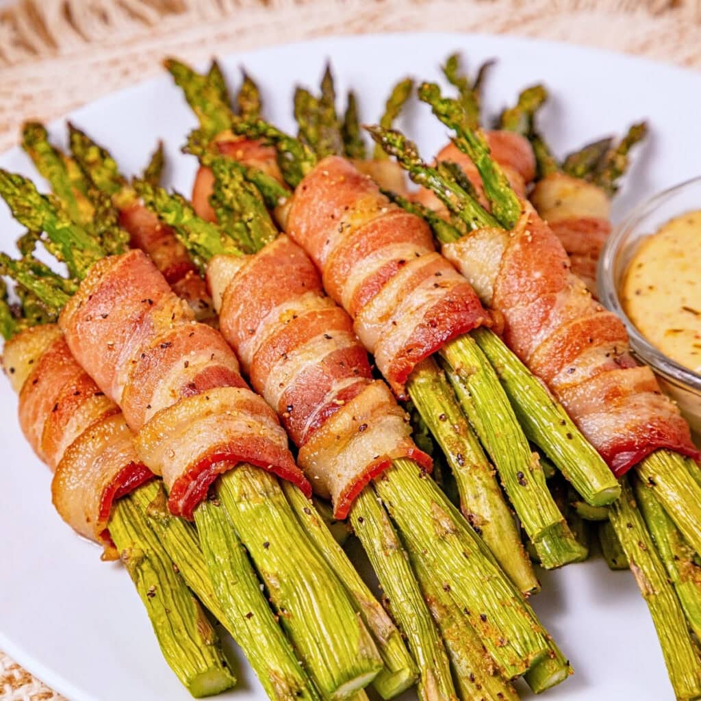 Bundles of asparagus wrapped in crispy bacon, served with a dipping sauce.
