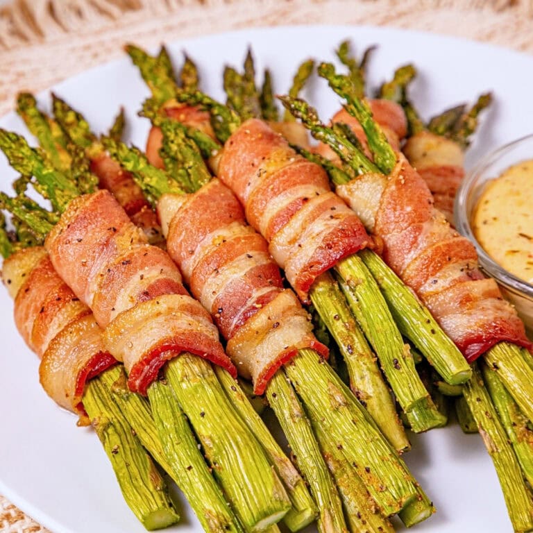 Bundles of asparagus wrapped in crispy bacon, served with a dipping sauce.