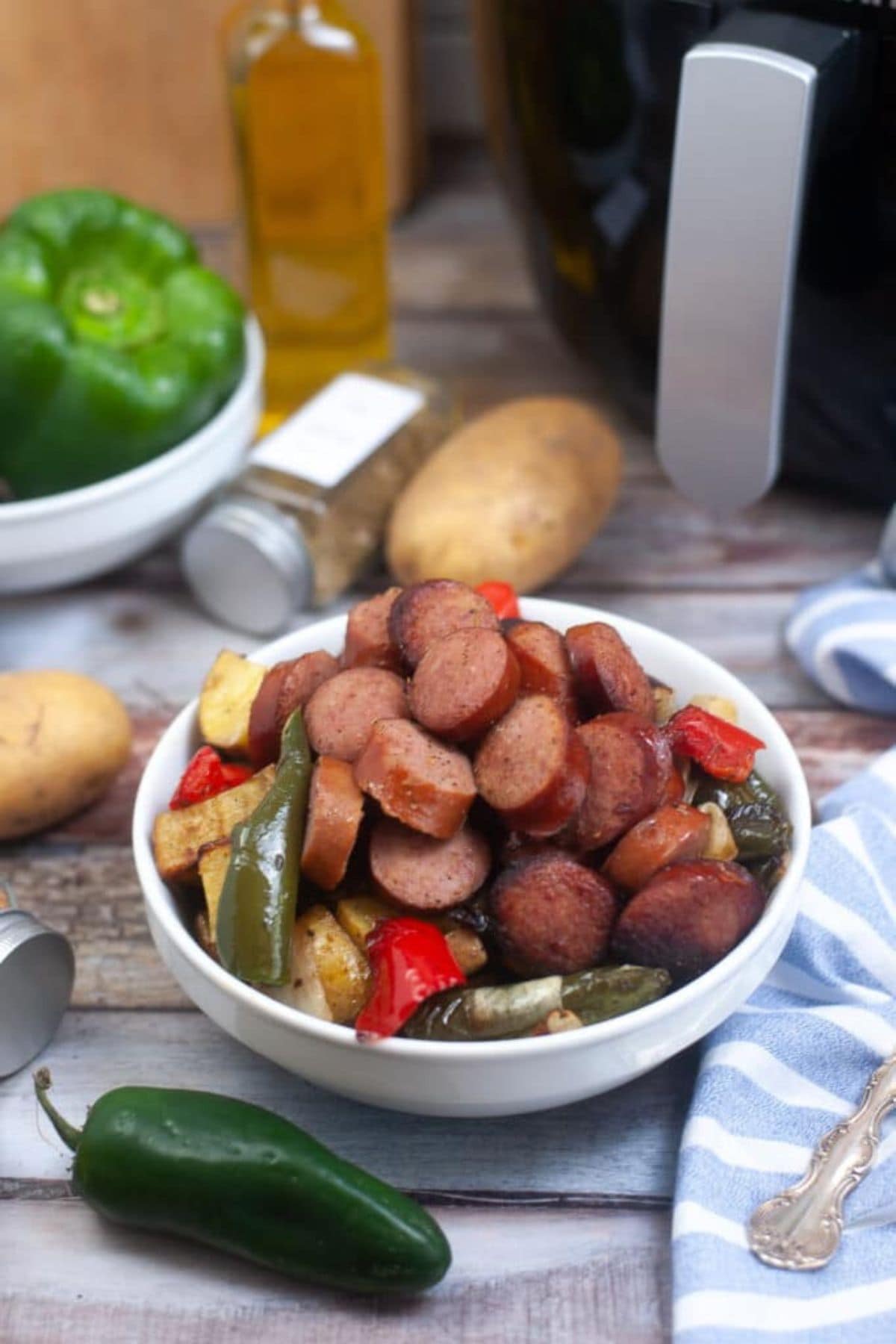 Bowl of kielbasa sausage meals with roasted peppers and potatoes on rustic table.