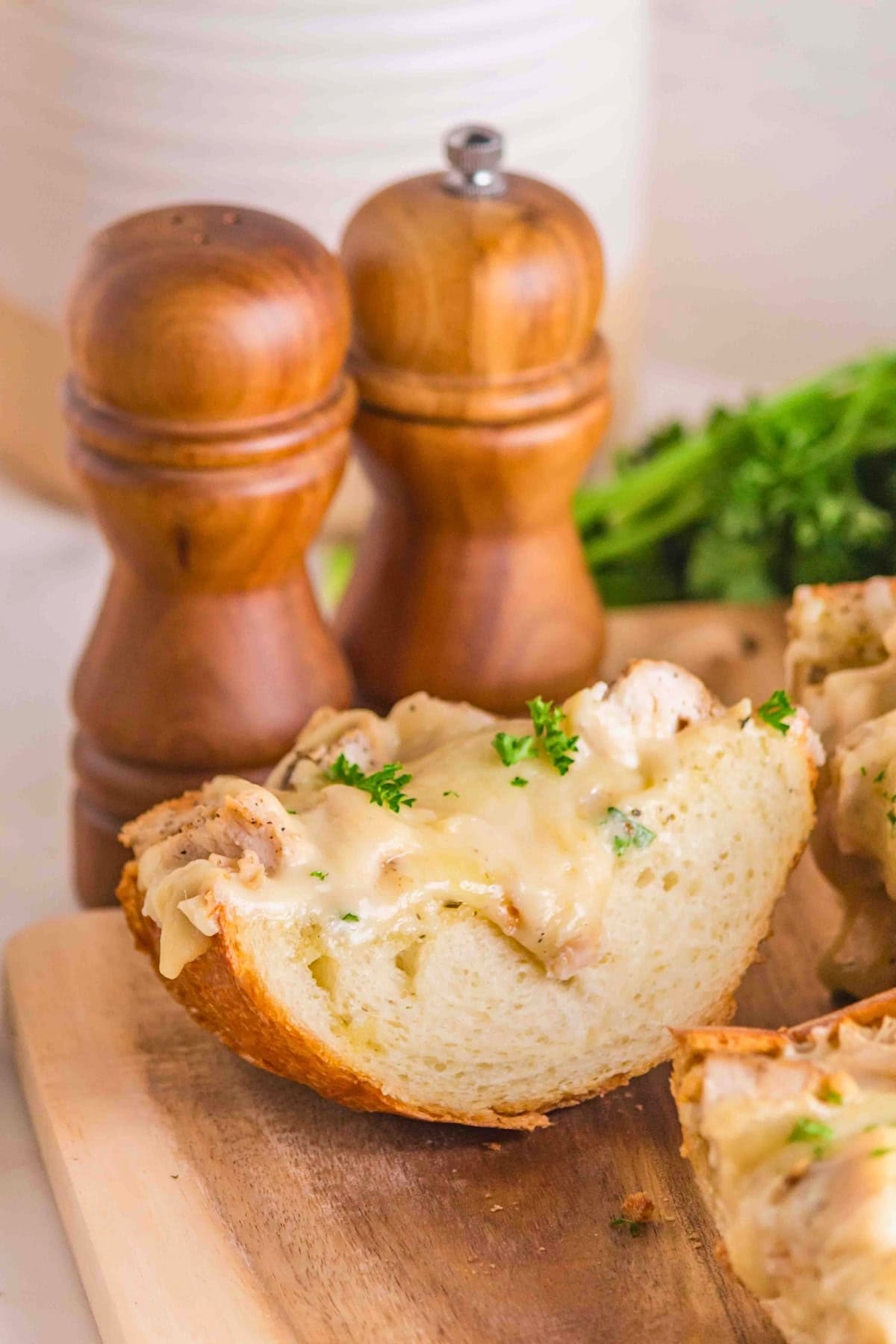 A slice of cheesy bread with herbs on a wooden board, next to salt and pepper shakers.