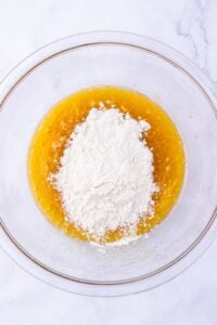Clear glass bowl with flour and wet ingredients on a marble surface.