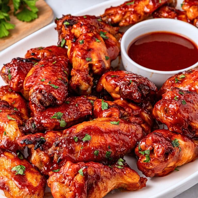 Plate of saucy barbecue chicken wings with a cup of dipping sauce.