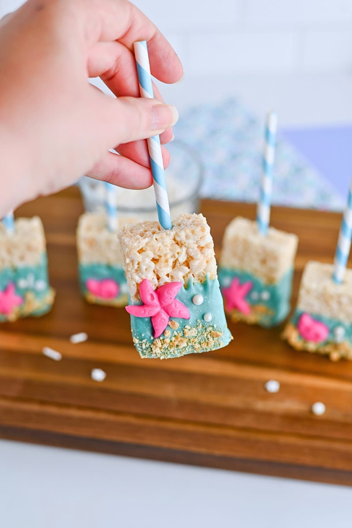Hand holding a decorated Rice Krispies treat pop with blue and pink sea-themed designs.