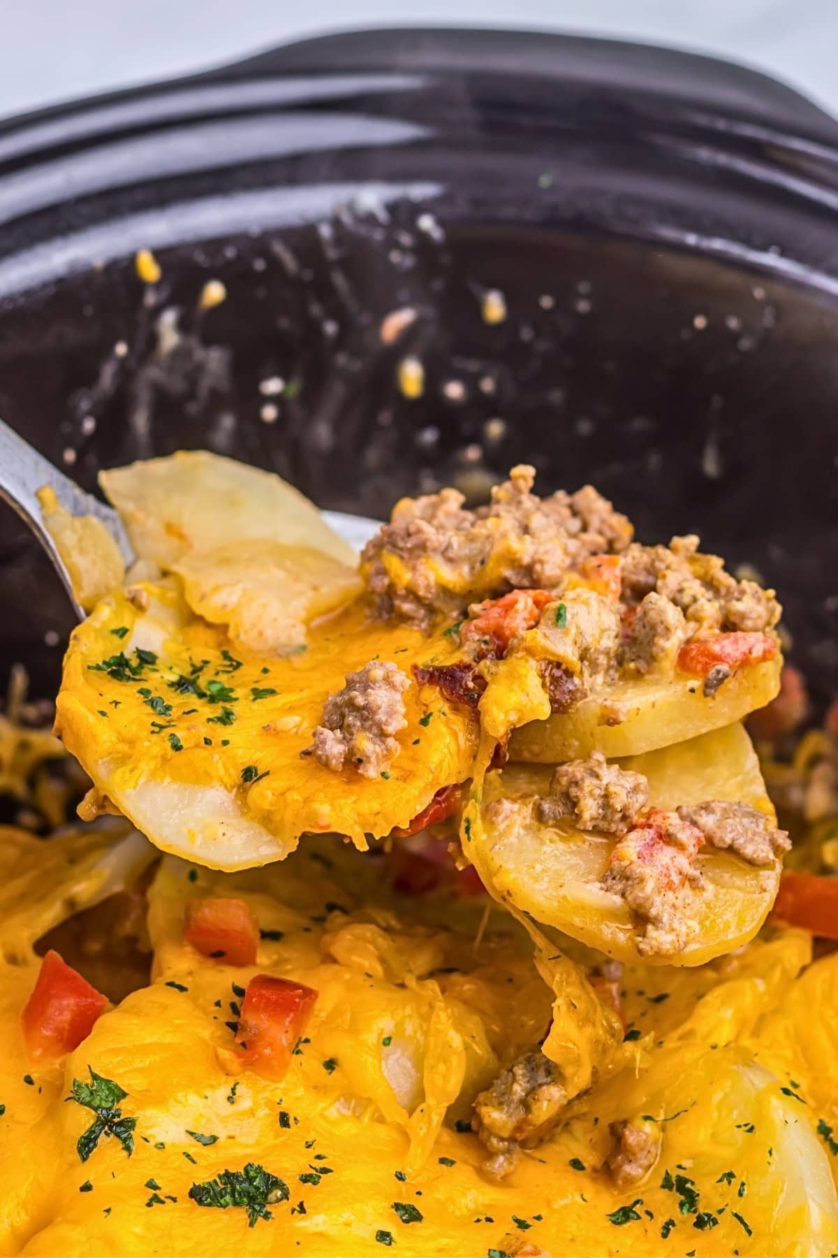 A spoonful of cheesy beef and potato casserole being served from a slow cooker.