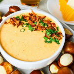 Cheese dip topped with bacon and green onions, surrounded by pretzel bites.