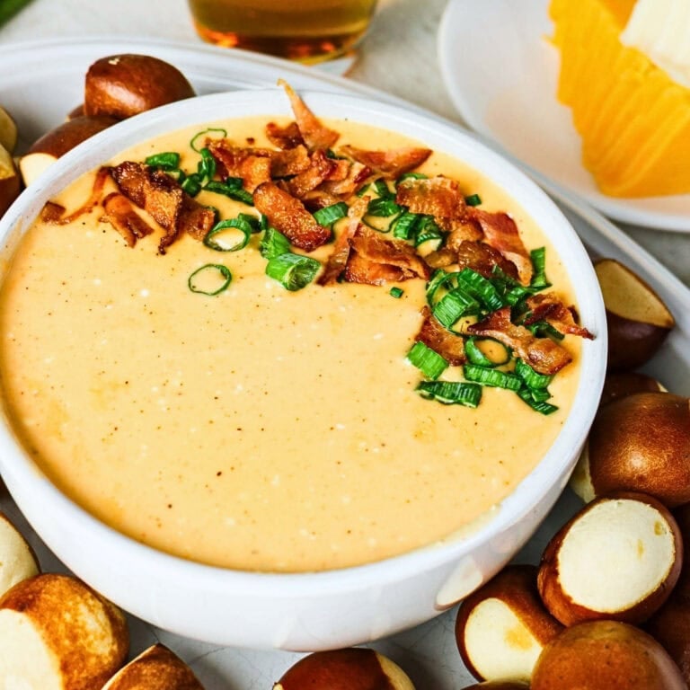 Cheese dip topped with bacon and green onions, surrounded by pretzel bites.
