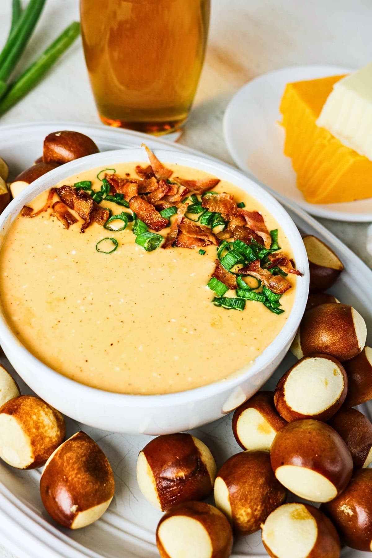 Bowl of cheese dip topped with bacon and green onions, with pretzel bites.