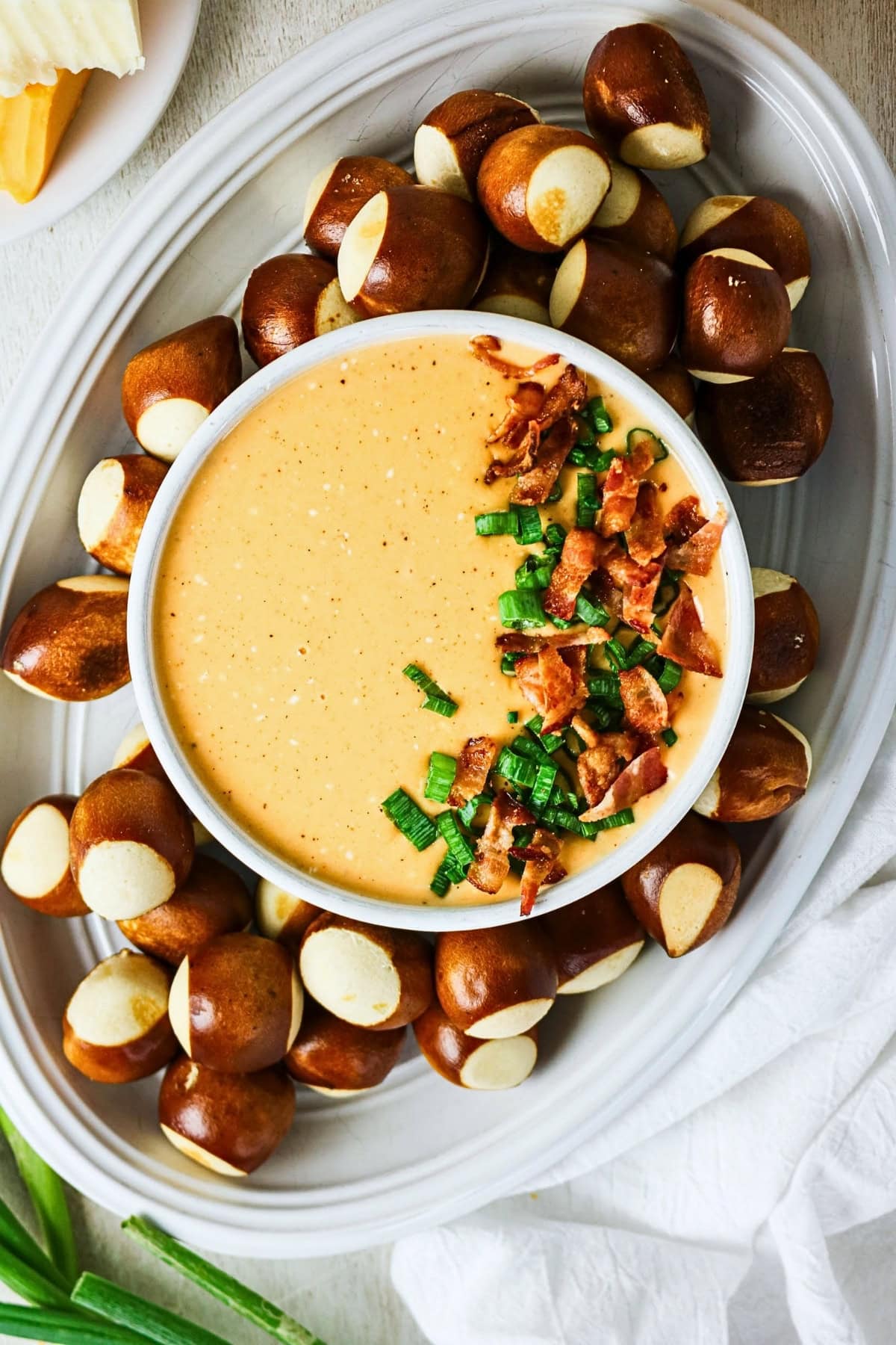 Cheese dip topped with bacon and green onions, surrounded by pretzel bites.