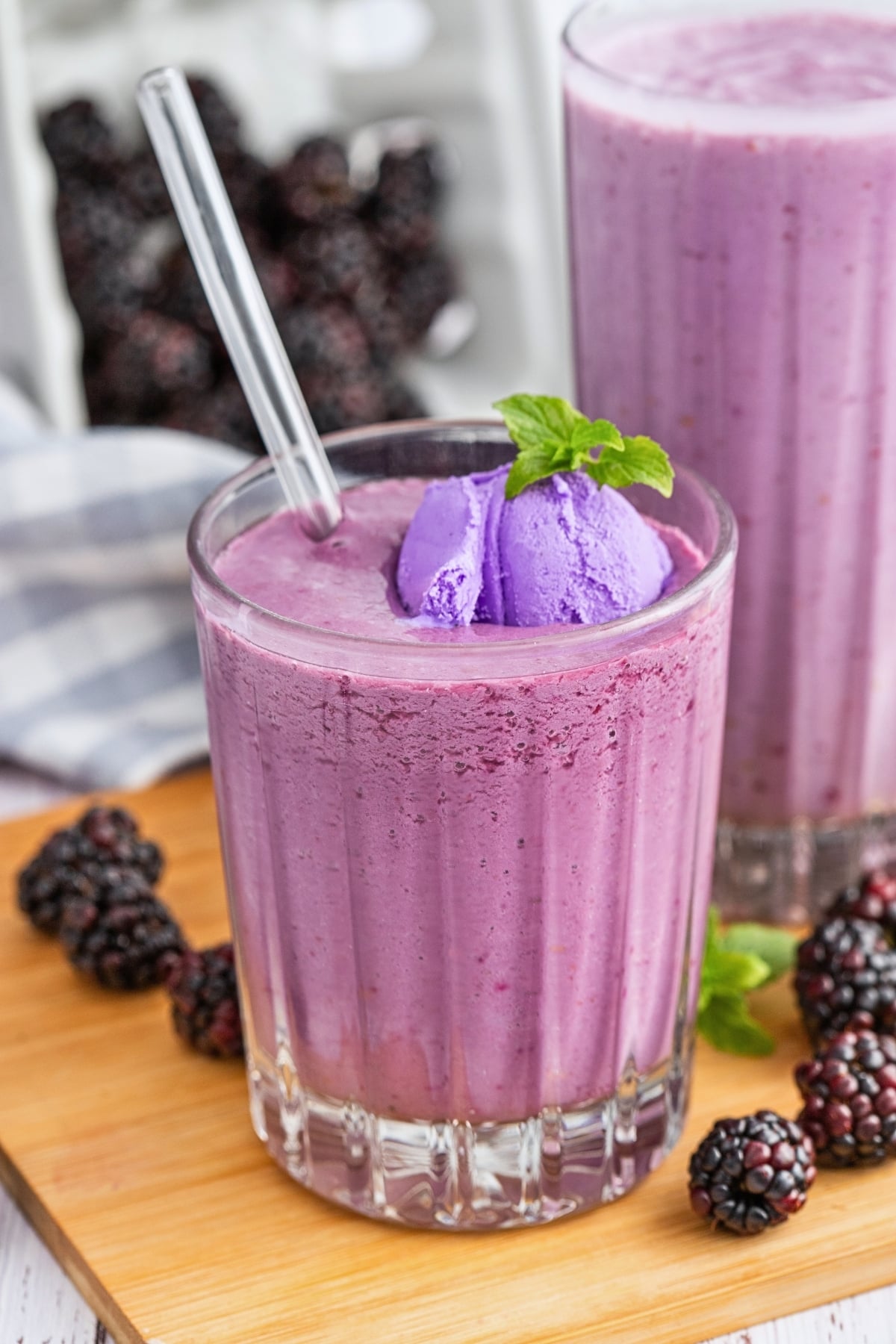 Purple smoothie with a scoop of ice cream and mint in a glass, surrounded by blackberries.