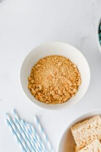 A white bowl filled with crushed graham crackers on a white surface.