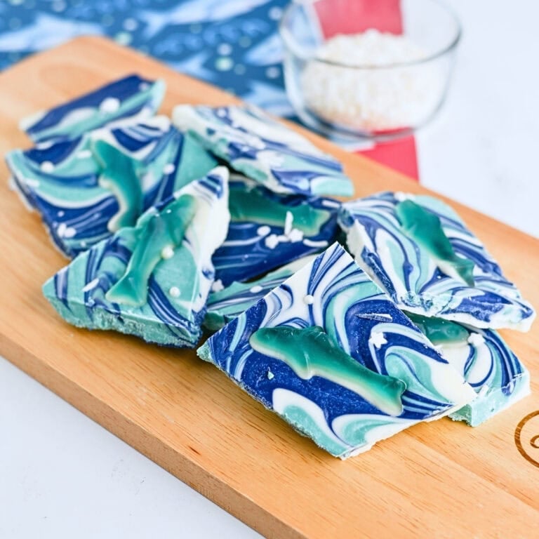 Swirled blue and white candy bark topped with gummy sharks on a wooden board.