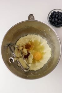 A mixing bowl with batter, an egg, and a bowl of blueberries nearby.