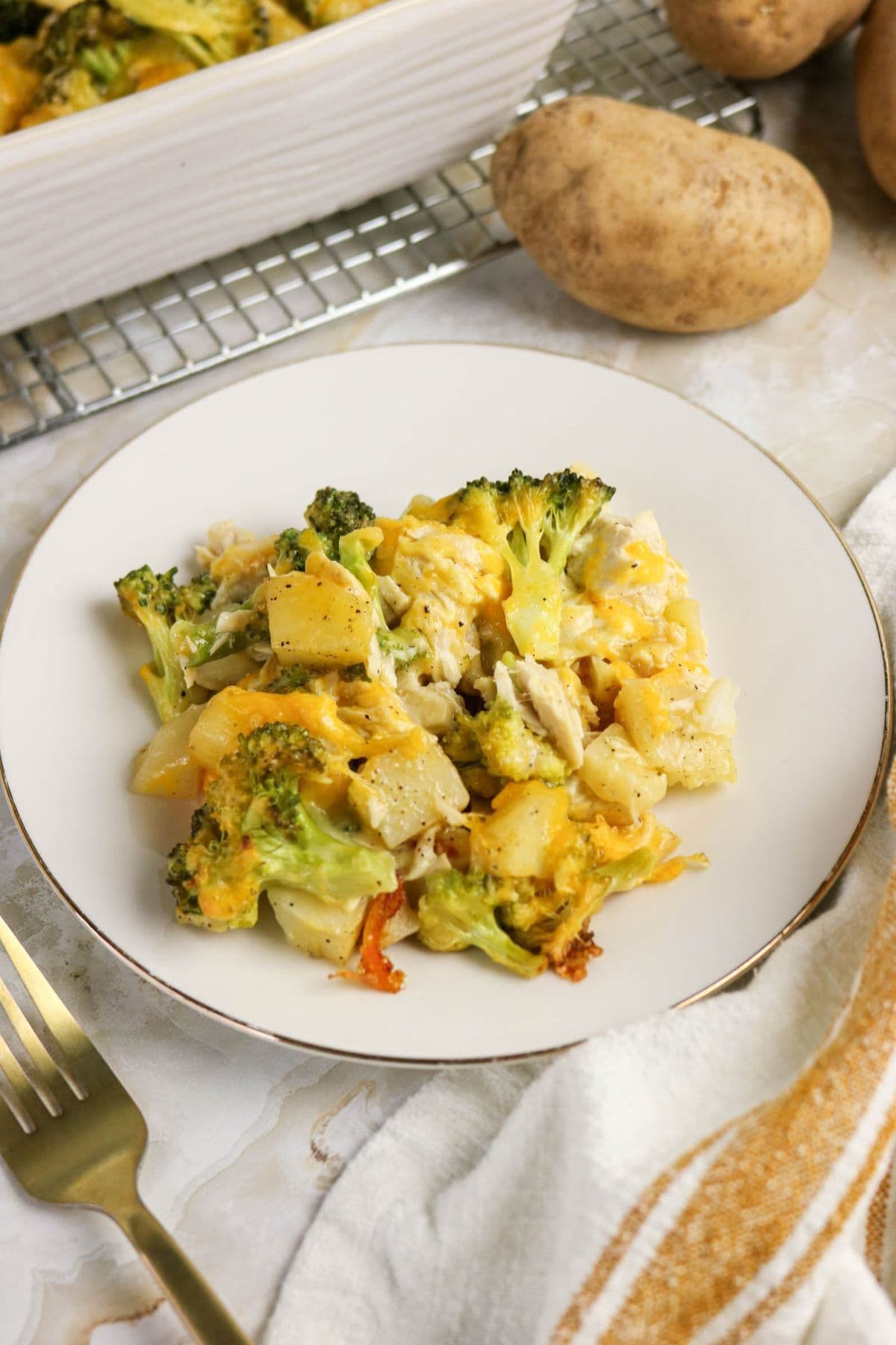A plate of cheesy broccoli, potato, and chicken casserole recipe on a white plate.