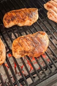 Seasoned chicken breasts grilling over hot coals on a barbecue grill.
