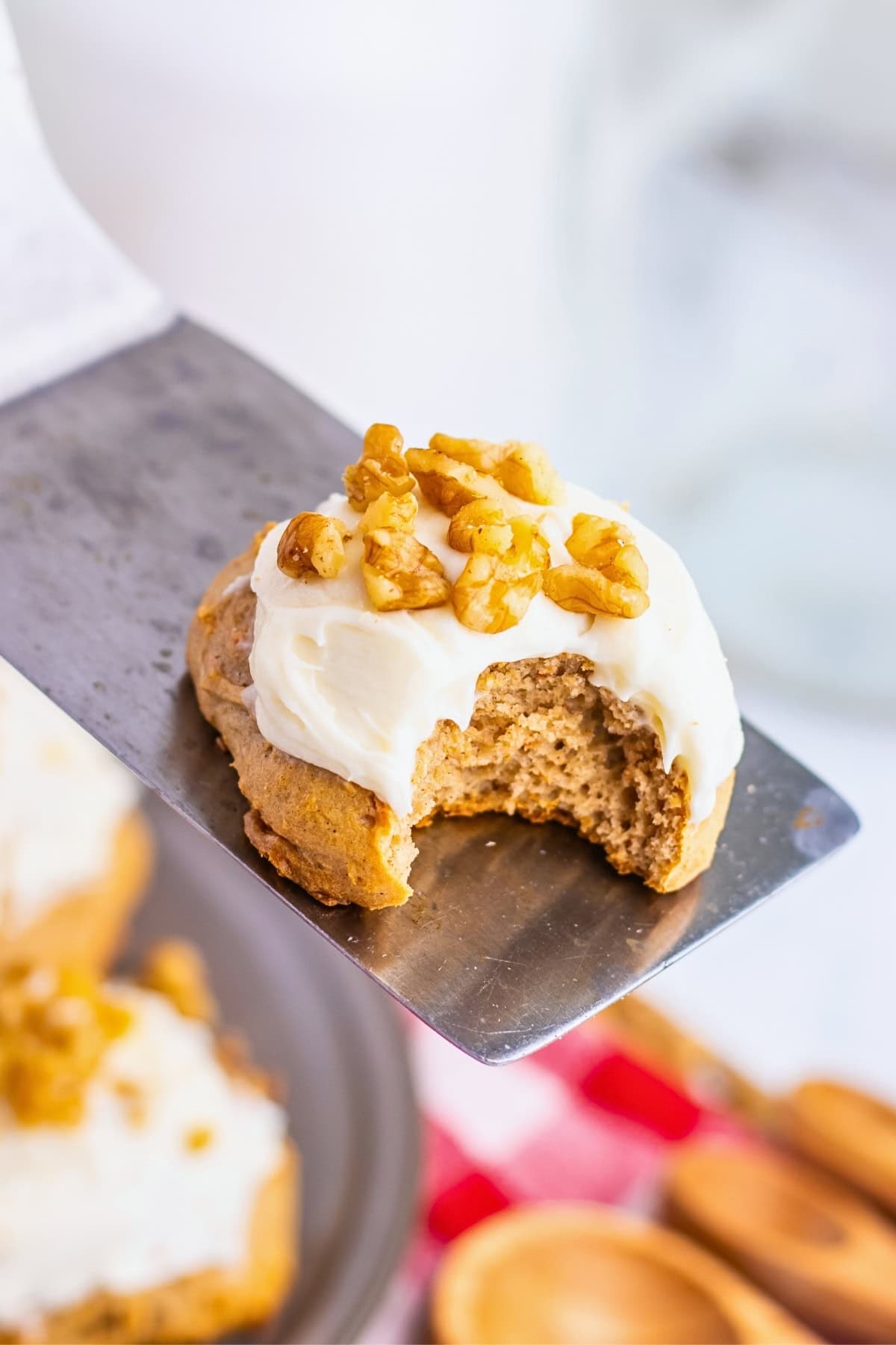 A frosted cookie with walnuts and a bite taken out, on a metal spatula.