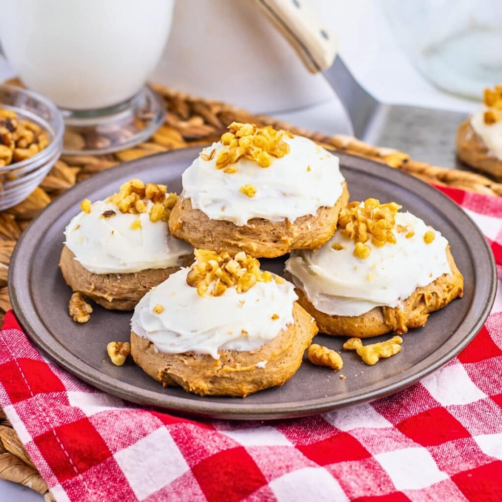 Four frosted cookies topped with chopped walnuts on a plate with a red plaid napkin.