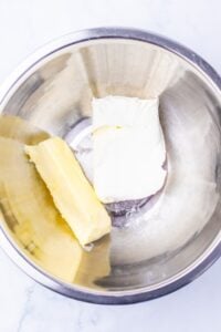A stick of butter and cream cheese in a stainless steel mixing bowl.