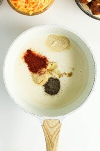 White saucepan with milk, spices, and seasonings, viewed from above.