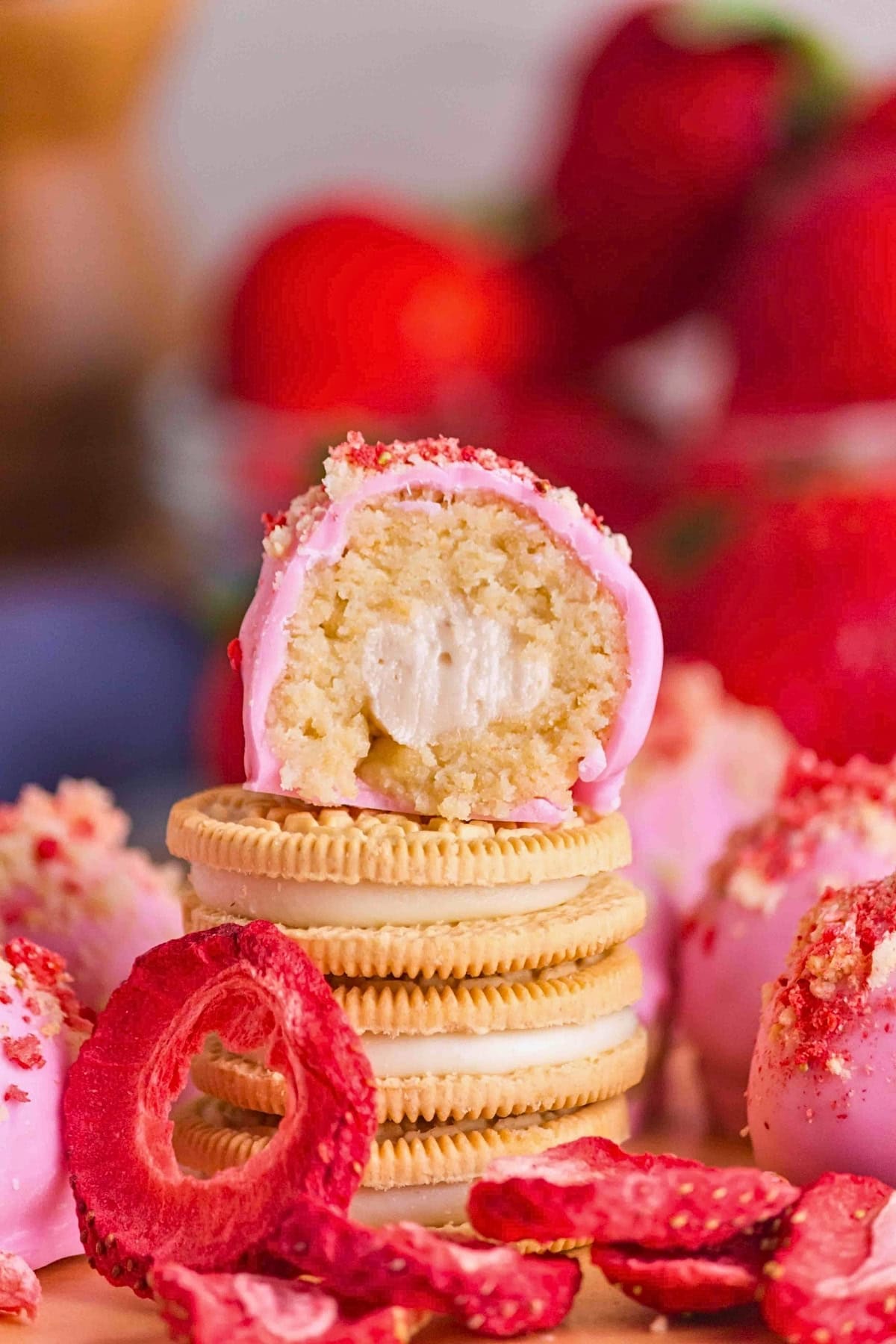 Stacked golden sandwich cookies with a pink-coated truffle, strawberries nearby.