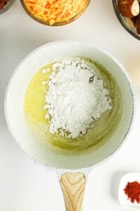 Flour and melted butter in a white pan, with cheese and spices nearby.