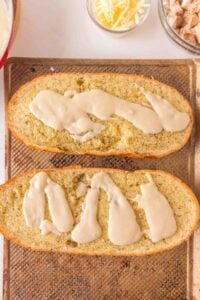Two slices of bread topped with a creamy white sauce on a baking sheet.
