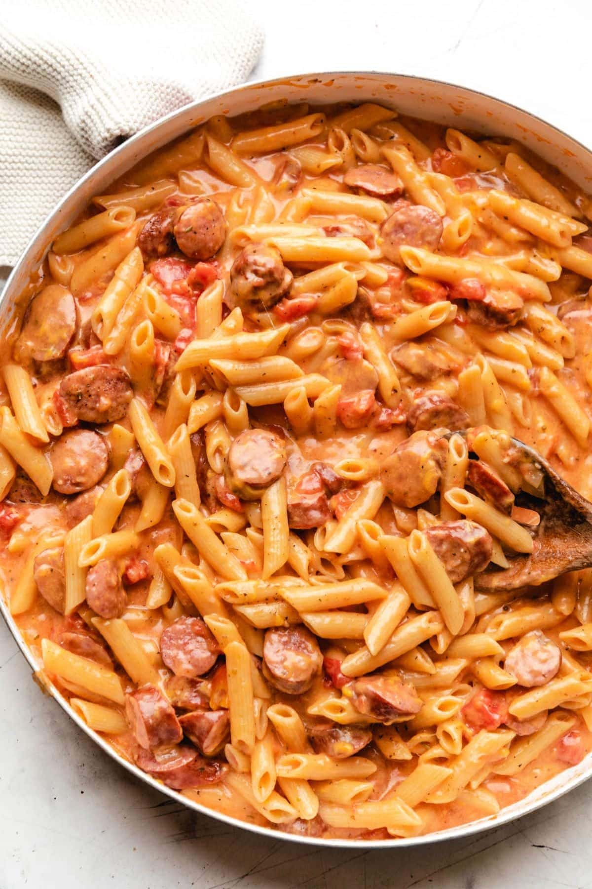 Creamy penne pasta with kielbasa sausage and diced tomatoes in a skillet.