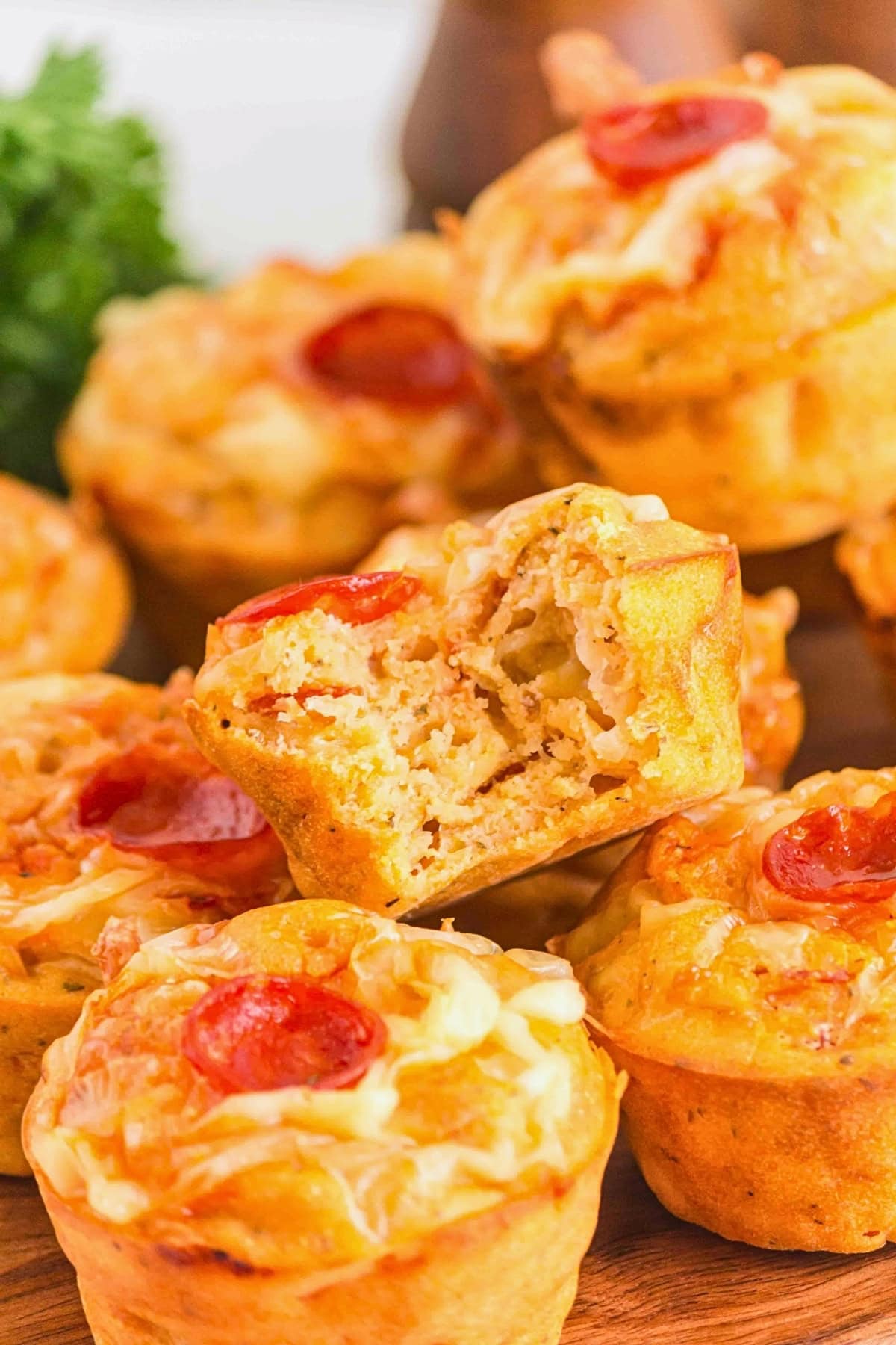 Mini pizza muffins topped with cheese and pepperoni, with one muffin bitten.