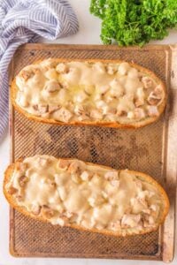 Two cheesy chicken French bread pizzas on a baking sheet, with parsley nearby.