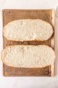 Two bread halves on a baking sheet, spread with a creamy herb mixture.
