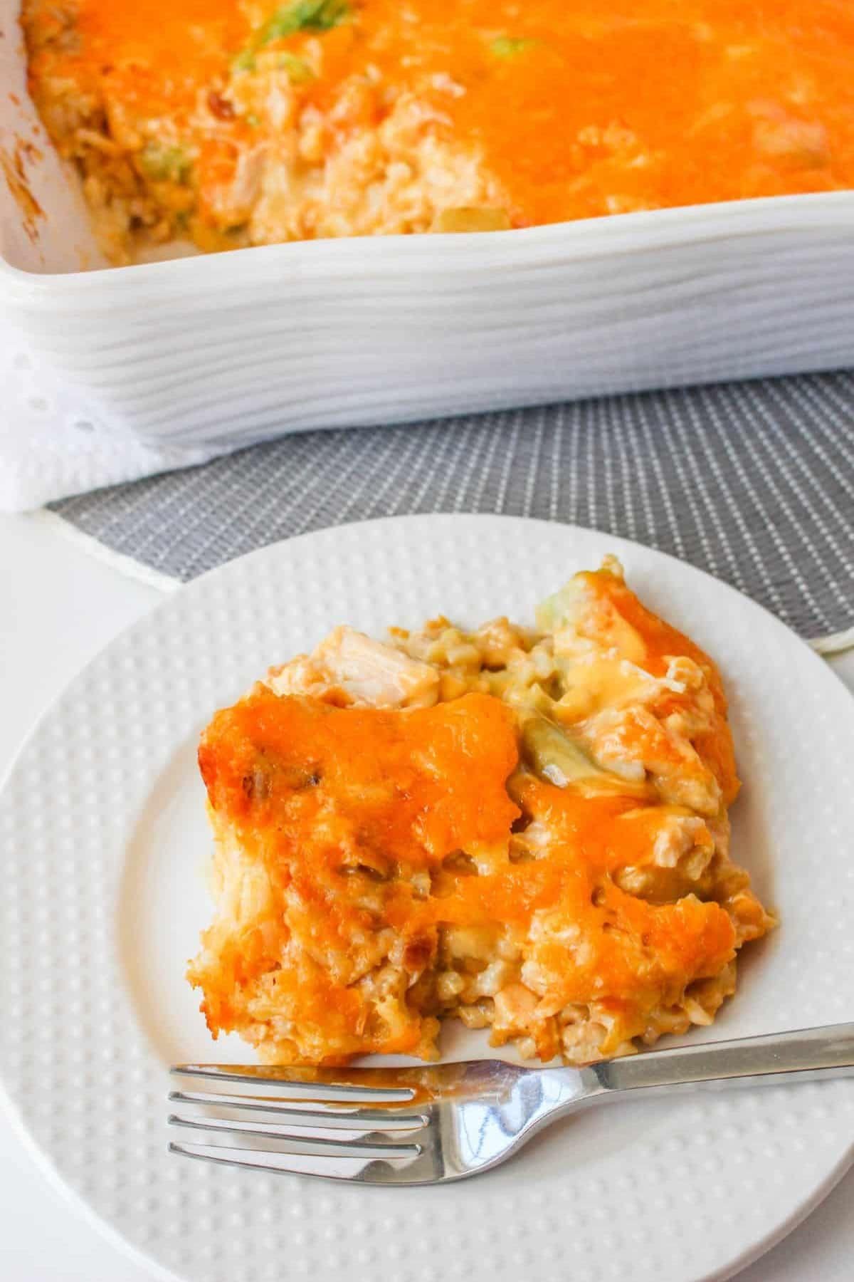 A serving of cheesy chicken casserole on a plate, casserole dish in background.