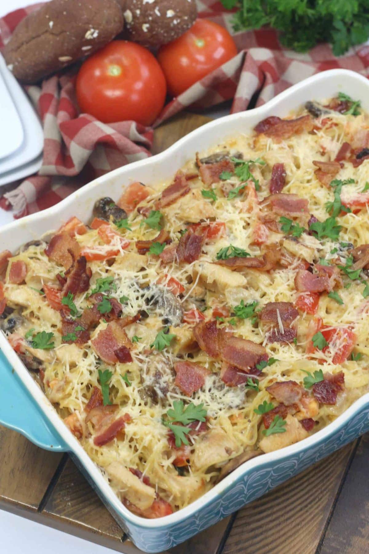 Baked chicken casserole topped with bacon, cheese, and herbs in a blue dish.
